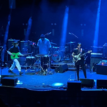 3 members of Dehd performing live on the Albert Hall stage bathed in blue light